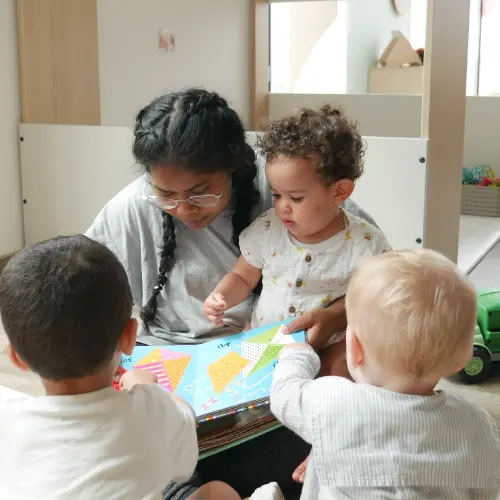 trois enfant regardant un livre avec une professionnelle de crèche